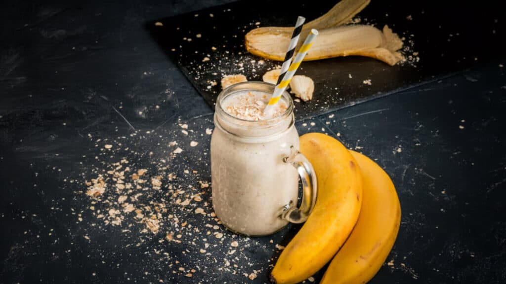 Smoothie de banana e manteiga de amendoim no fundo preto - uma bebida pós-treino nutritiva feita com banana, leite (ou leite à base de plantas), aveia, manteiga de amendoim, mel e gelo. Cremoso e repleto de nutrientes.